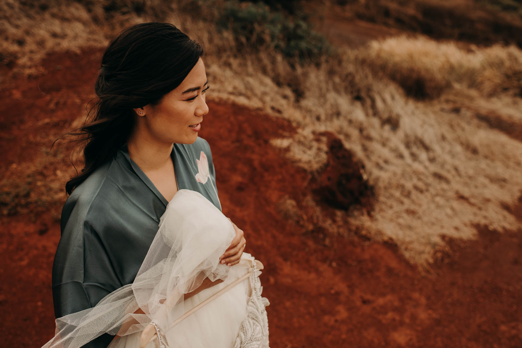 Alison, in a painted silk robe, holds the dress while standing in a red clay parking lot while looking off into the horizon.