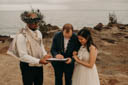 Euta holds paperwork that Andrew is signing while Alison holds onto his left arm.